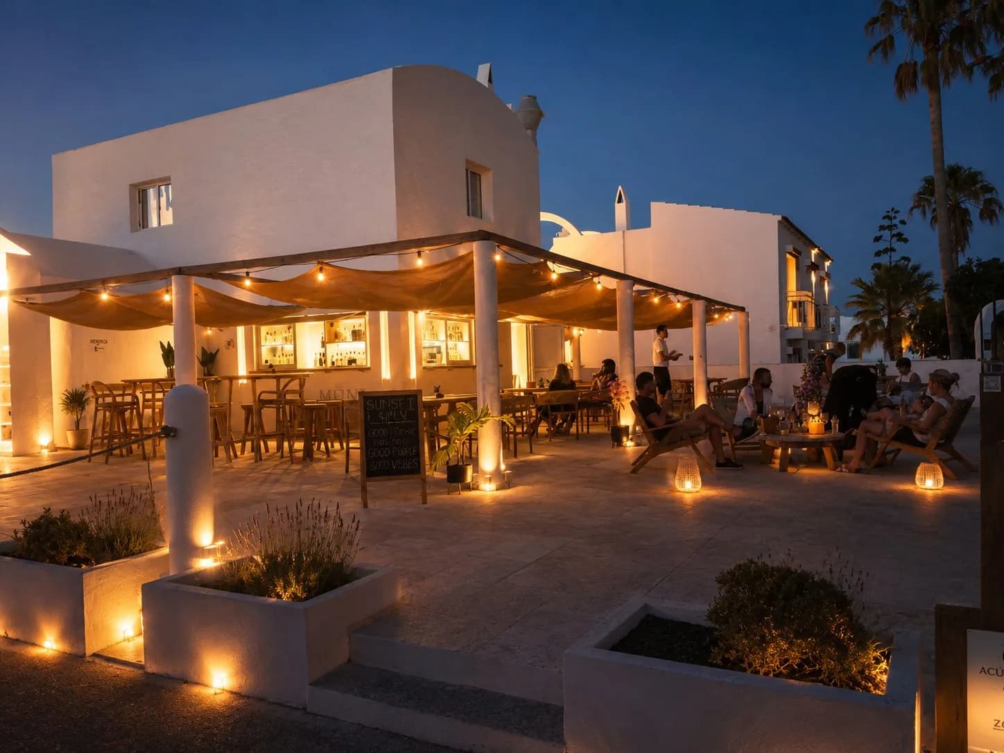 The MÖNA terrace at dusk: linen canopies, lanterns lit, guests gathered as the sky goes blue over Cala en Forcat